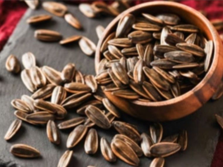 一個木碗裡盛著烤葵花籽,這些葵花籽散落在深色的石面上。