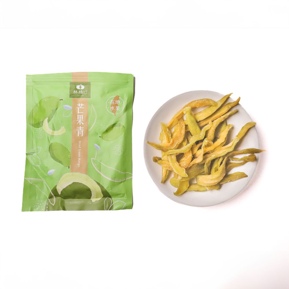 白色背景上的散落著芒果乾條，旁邊則是一個打開的綠色產品包裝袋。