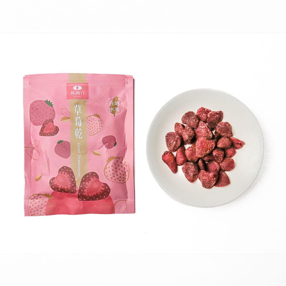 一個粉紅色的零食袋裡，冷凍乾燥草莓碎片散落在純白色的表面。