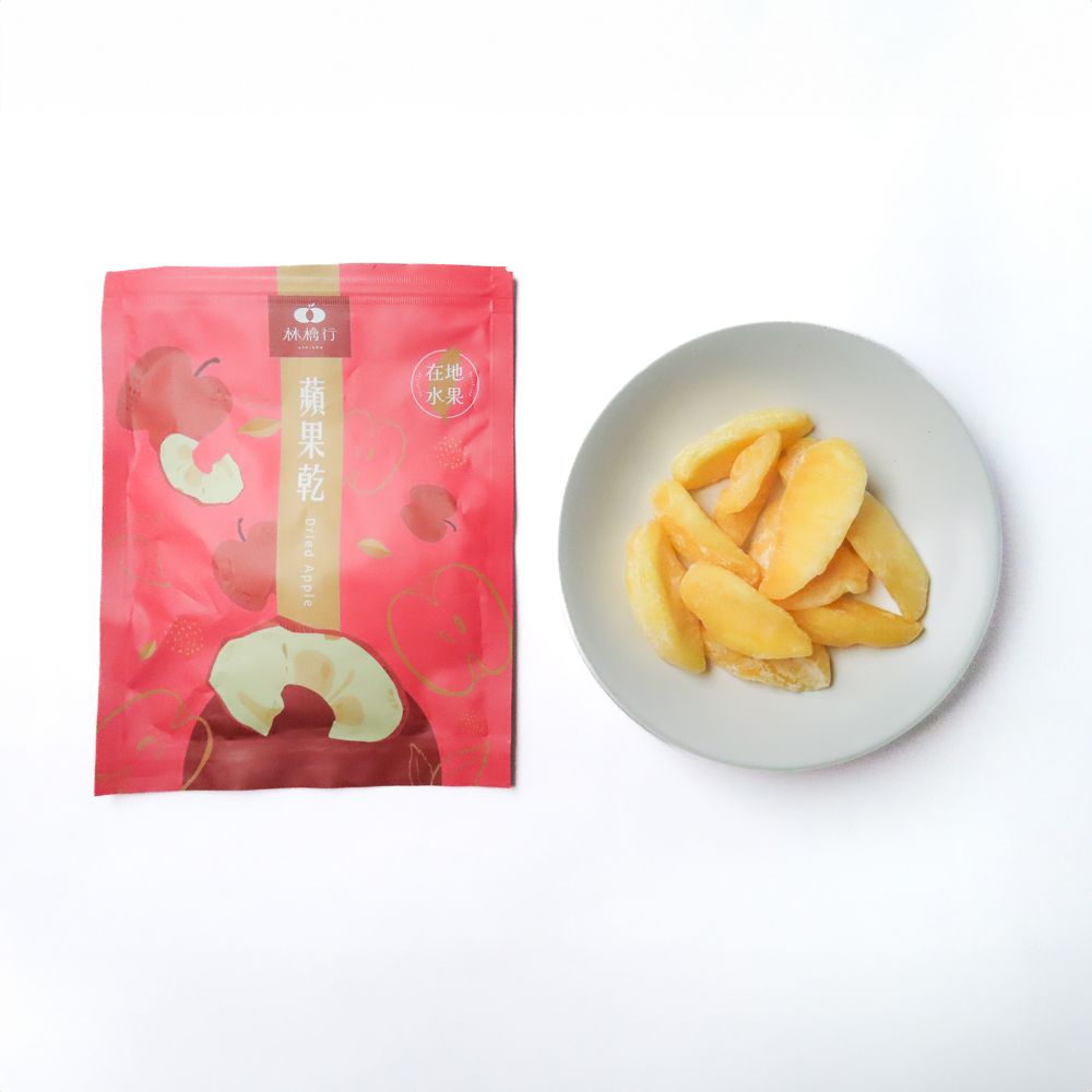 一袋粉紅色的蘋果乾片側翻在地，幾塊黃色的蘋果乾散落在白色的表面上。