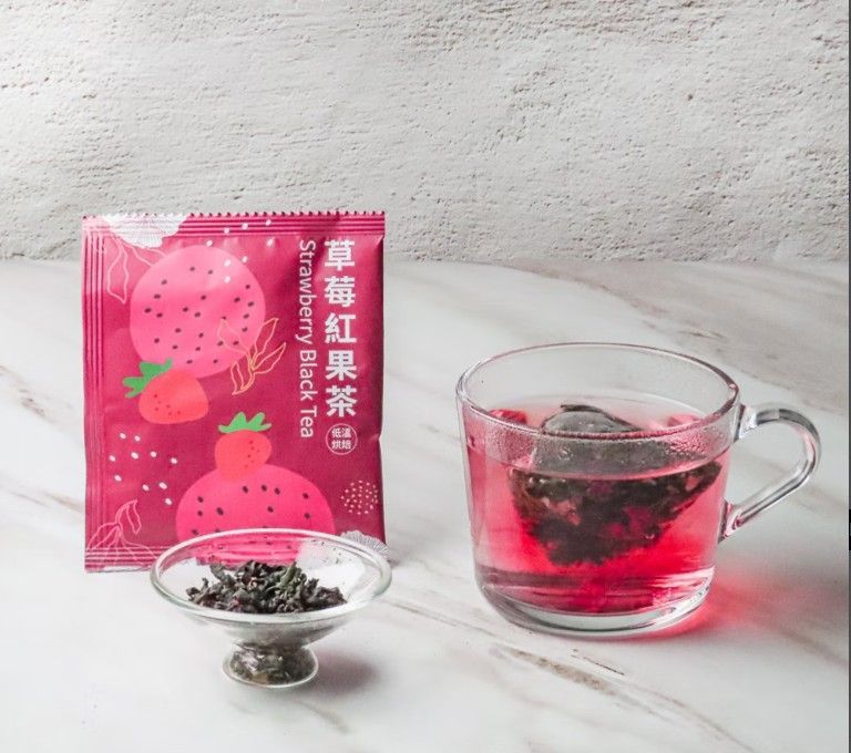 桌上放著一包草莓紅茶、一小碟乾茶葉和一杯泡好的紅茶。