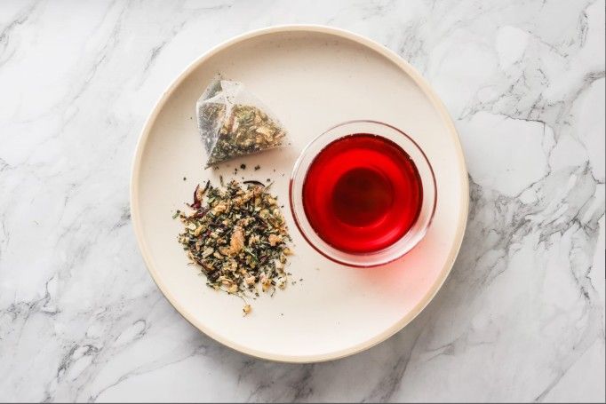 一包鳳梨洛神花茶、一杯泡好的紅茶和一小碟散裝茶葉，擺在大理石檯面上。