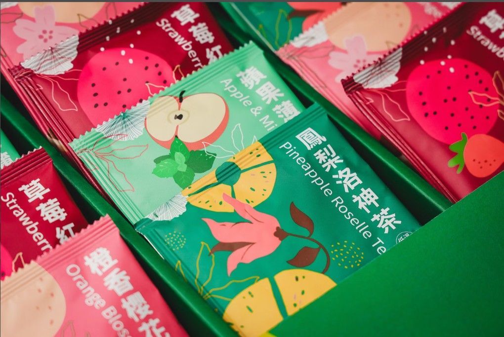 特寫鏡頭展示了一個充滿色彩鮮豔、圖案各異的茶包的禮盒，茶包上印有水果和花卉圖案。