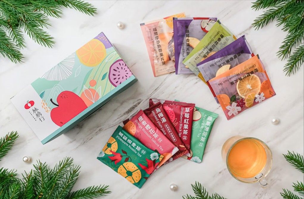 一個禮盒裡擺放著色彩繽紛、印有水果圖案的茶包，放在一張飾有綠植和珍珠的白色桌子上。