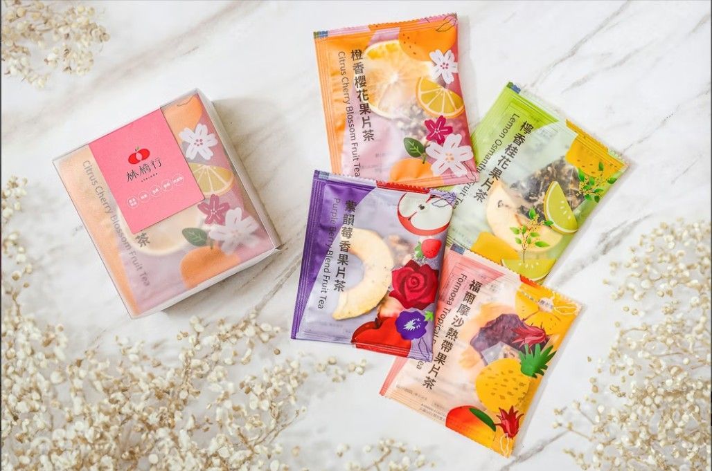 白色背景上的粉紅色禮盒旁擺放著四袋色彩鮮豔的乾果花茶混合物。