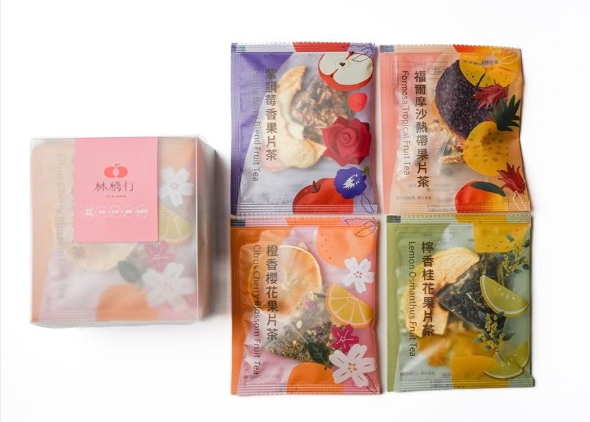 白色背景上的粉紅色禮盒旁擺放著四袋色彩鮮豔的乾果花茶混合物。
