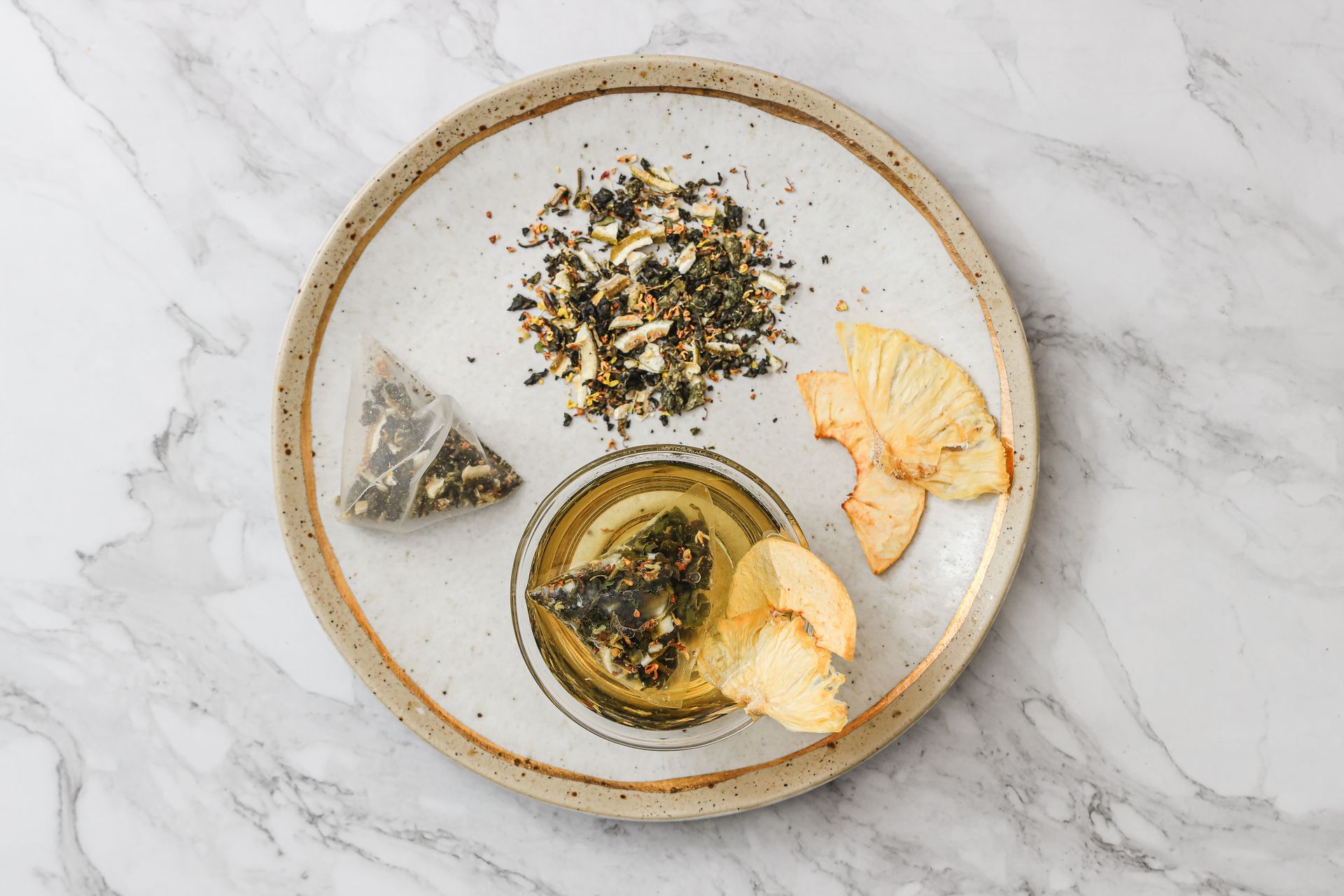 大理石桌上放著一個裝滿花草茶的玻璃茶壺，旁邊還有茶葉包、乾果片和一小杯茶。