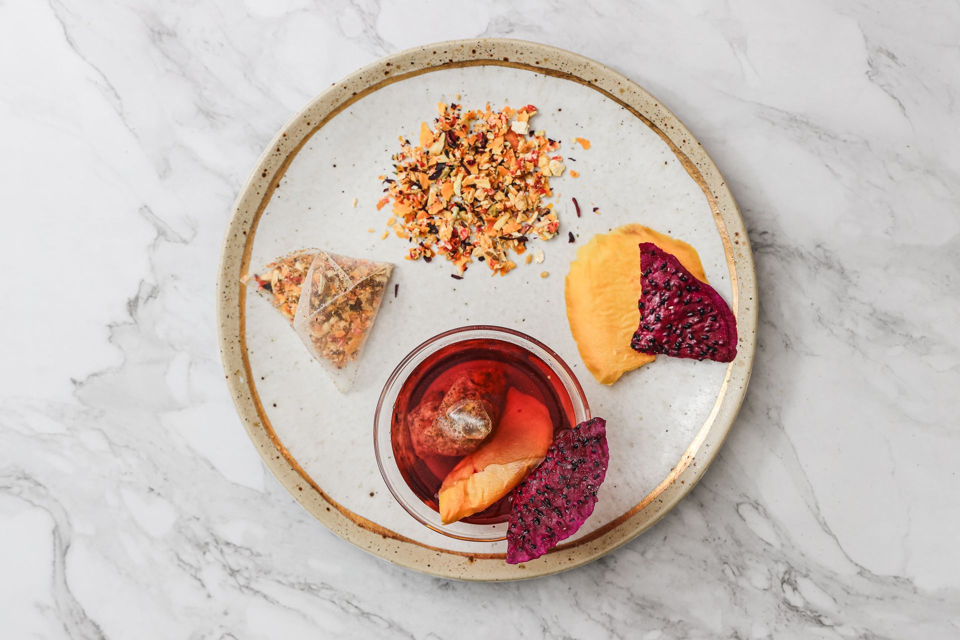 一個裝滿鮮紅色茶葉的玻璃茶壺放在大理石桌上，旁邊還有兩包茶葉、散裝茶葉和乾果片。