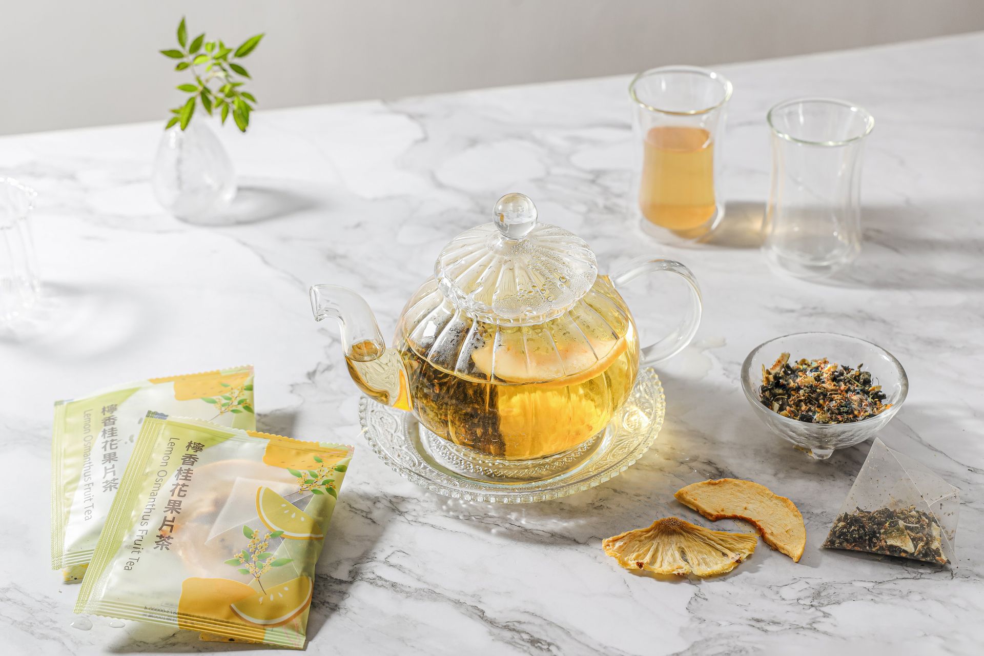 大理石桌上放著一個裝滿花草茶的玻璃茶壺，旁邊還有茶葉包、乾果片和一小杯茶。