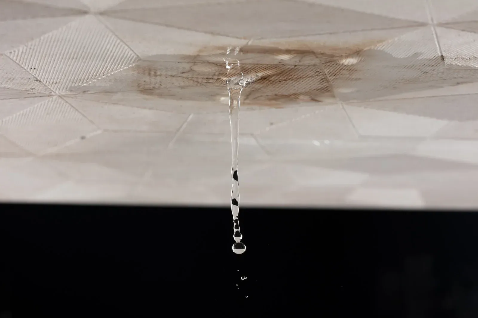 Water dripping from a stained ceiling against a dark background