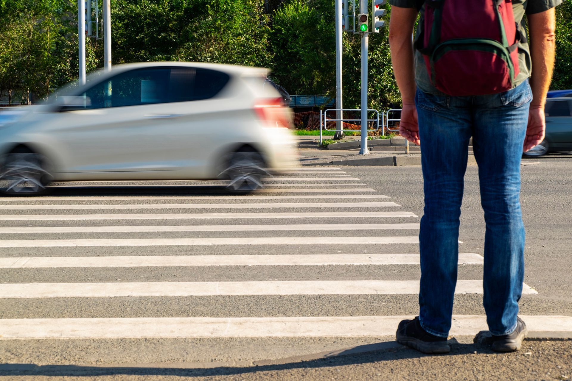Person standing at crosswalk as car speeds by. 