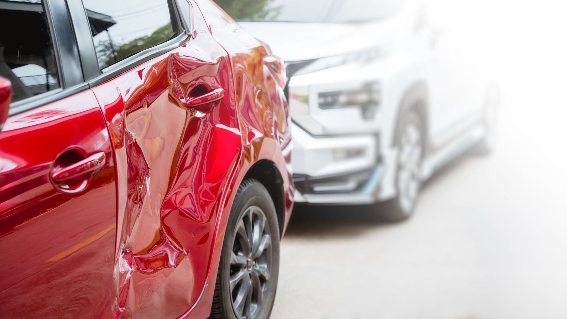Red car with rear-end damage, white SUV in background. 
