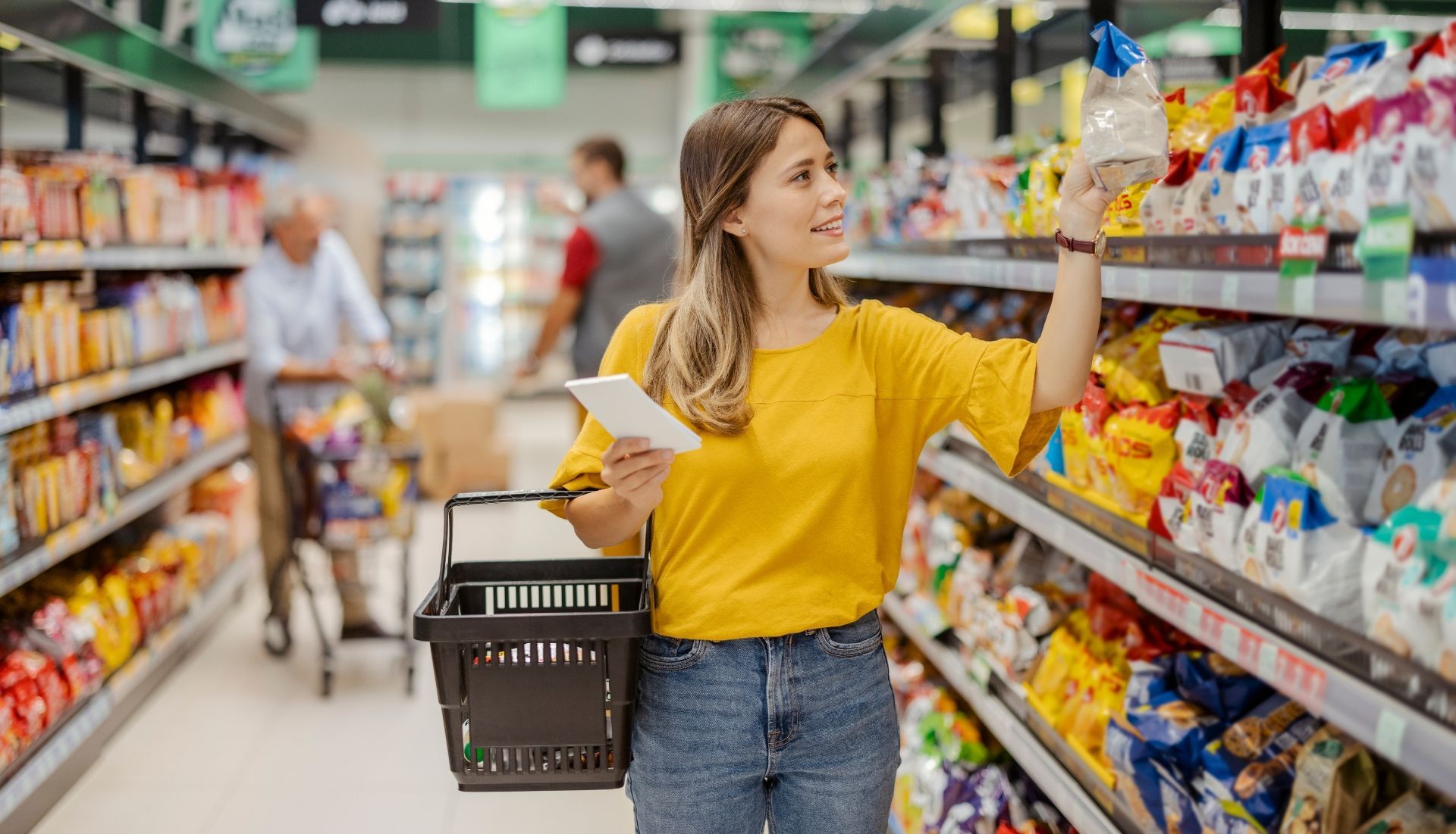 A woman is shopping in a supermarket while holding a basket.