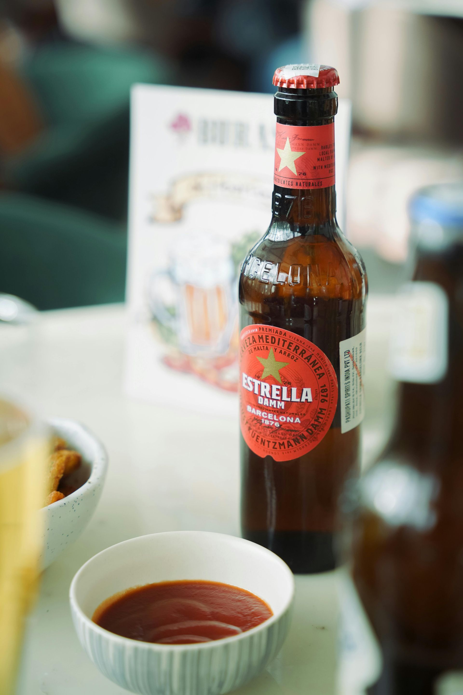 A bottle of estrella beer is sitting on a table next to a bowl of sauce.