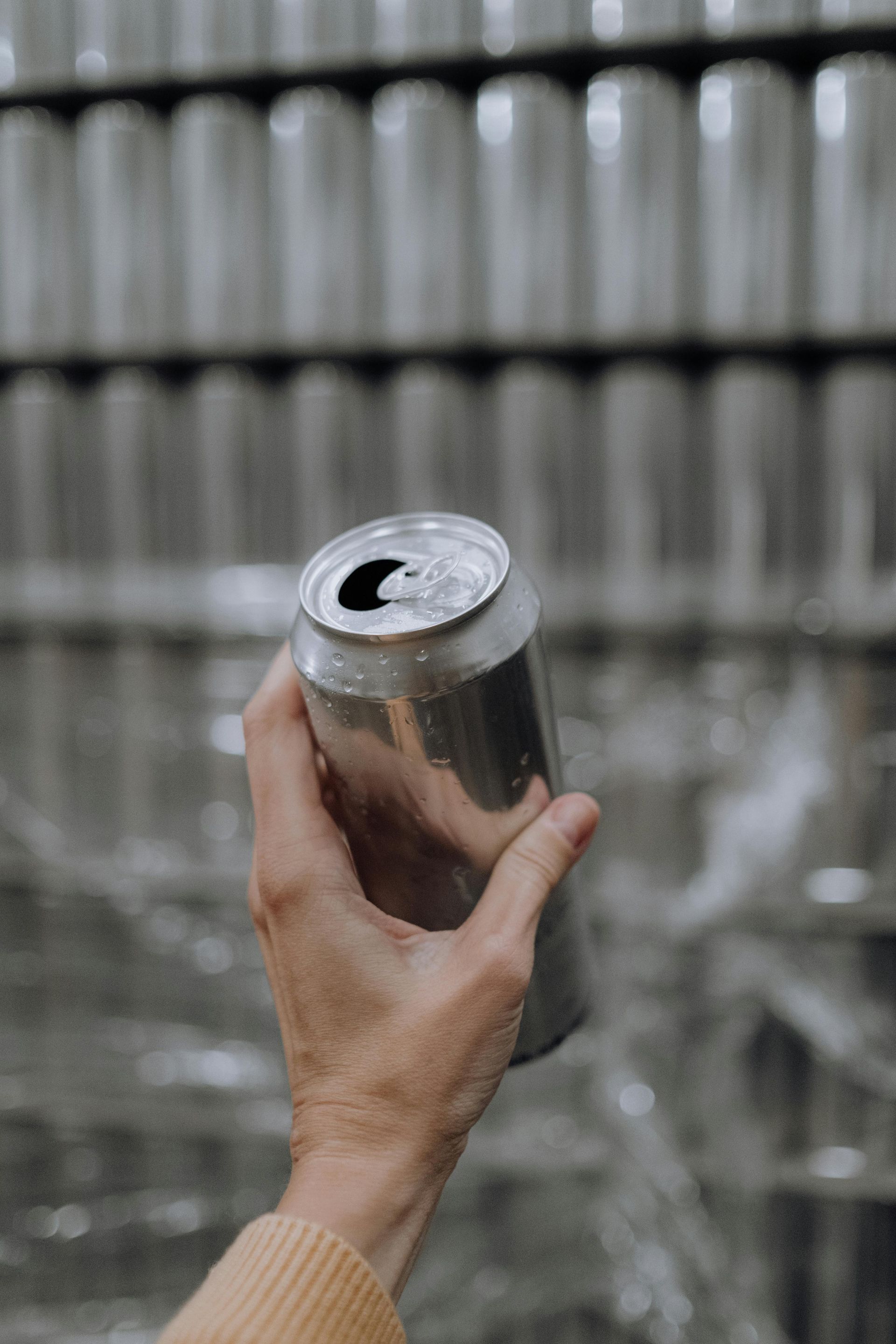 A person is holding a can of soda in their hand in front of a row of cans.