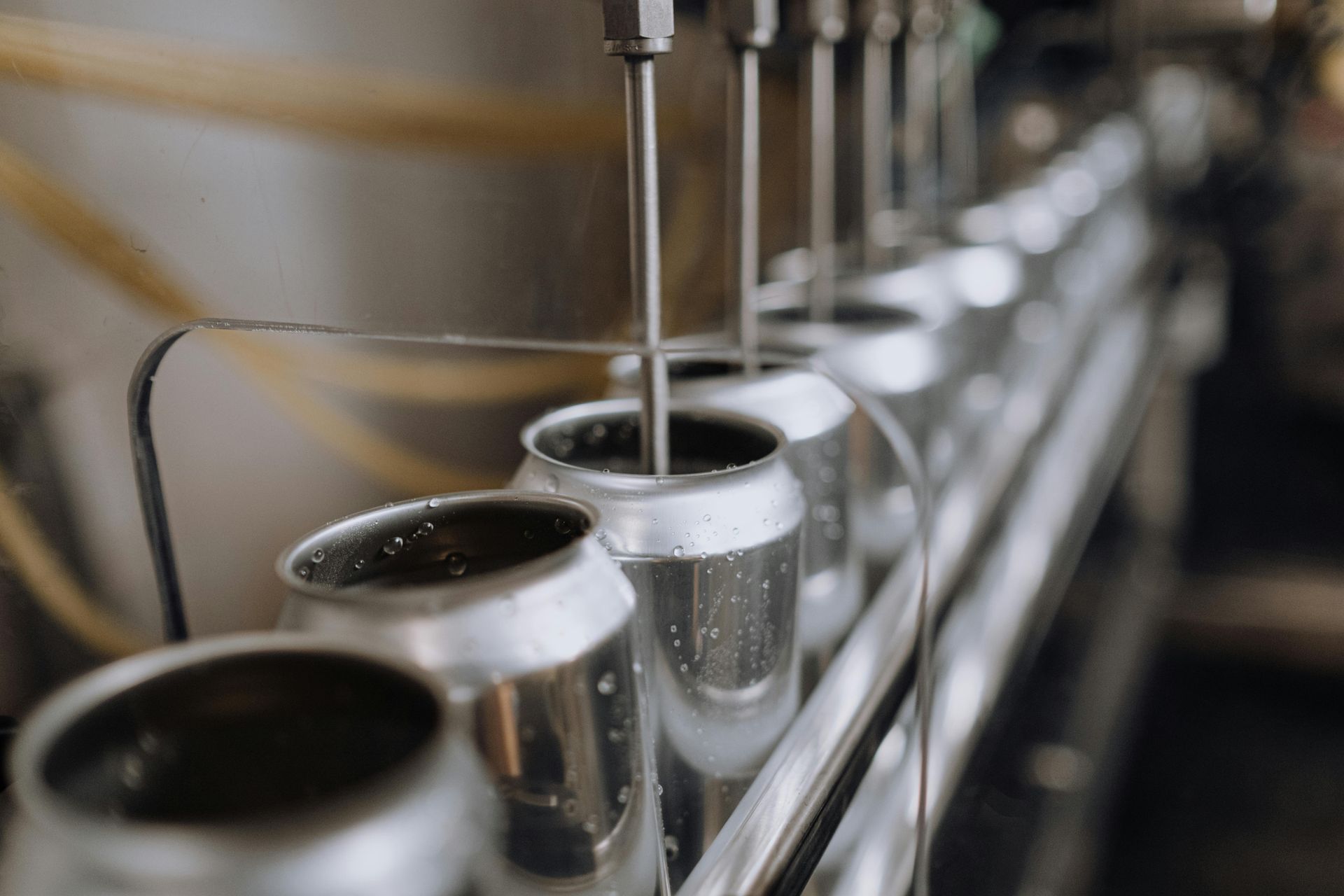 A row of cans are being filled with liquid on a conveyor belt.