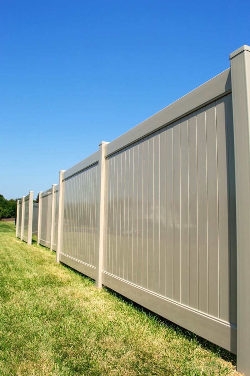 PVC fence running across a yard with blue sky in the background.