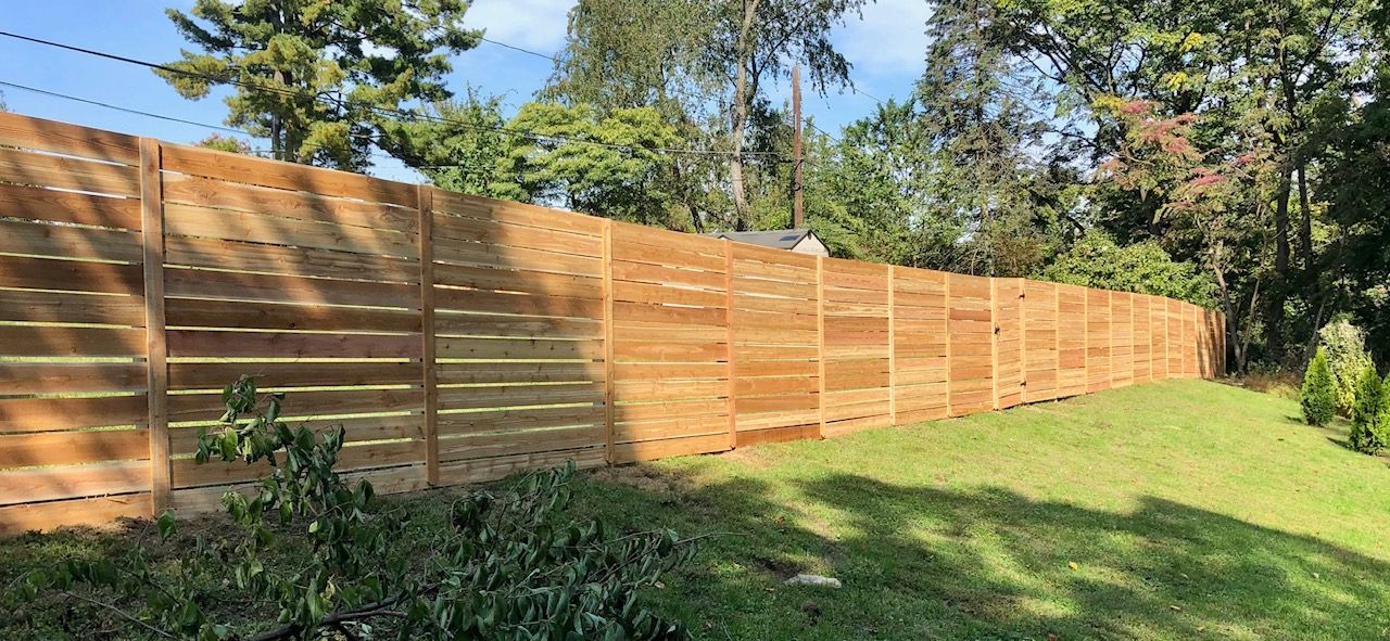 A wooden fence is surrounded by trees and grass in a backyard.