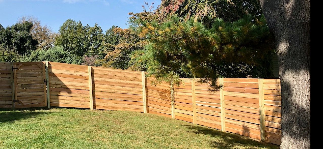 A wooden fence is in the middle of a lush green yard.