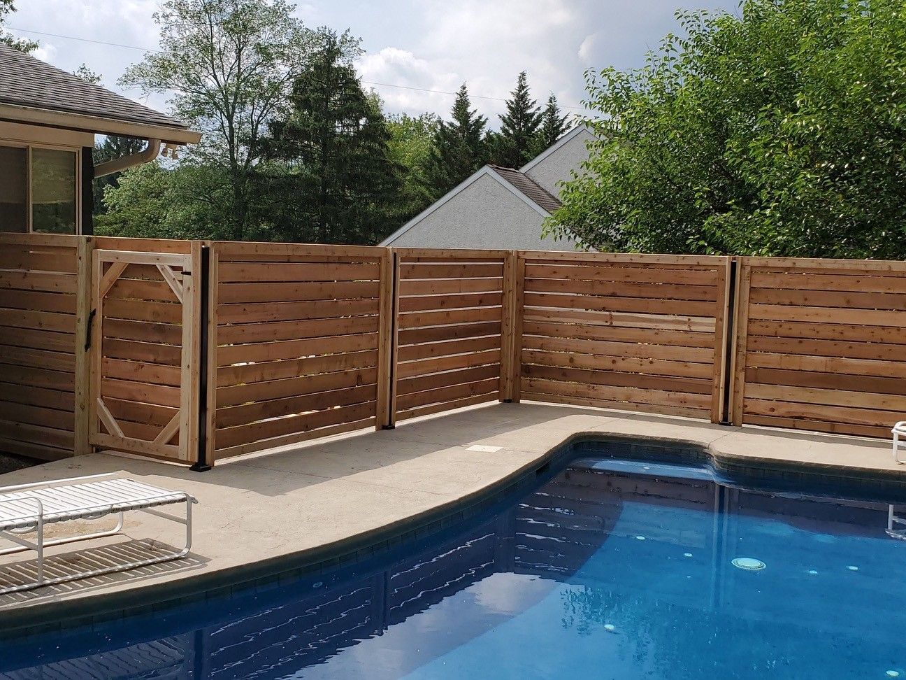 A wooden fence surrounds a large swimming pool.