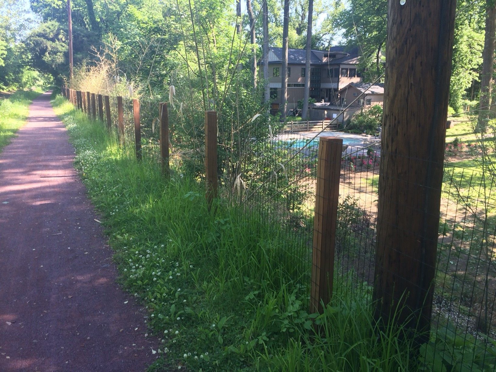 A wooden fence along a path in the woods with a house in the background.