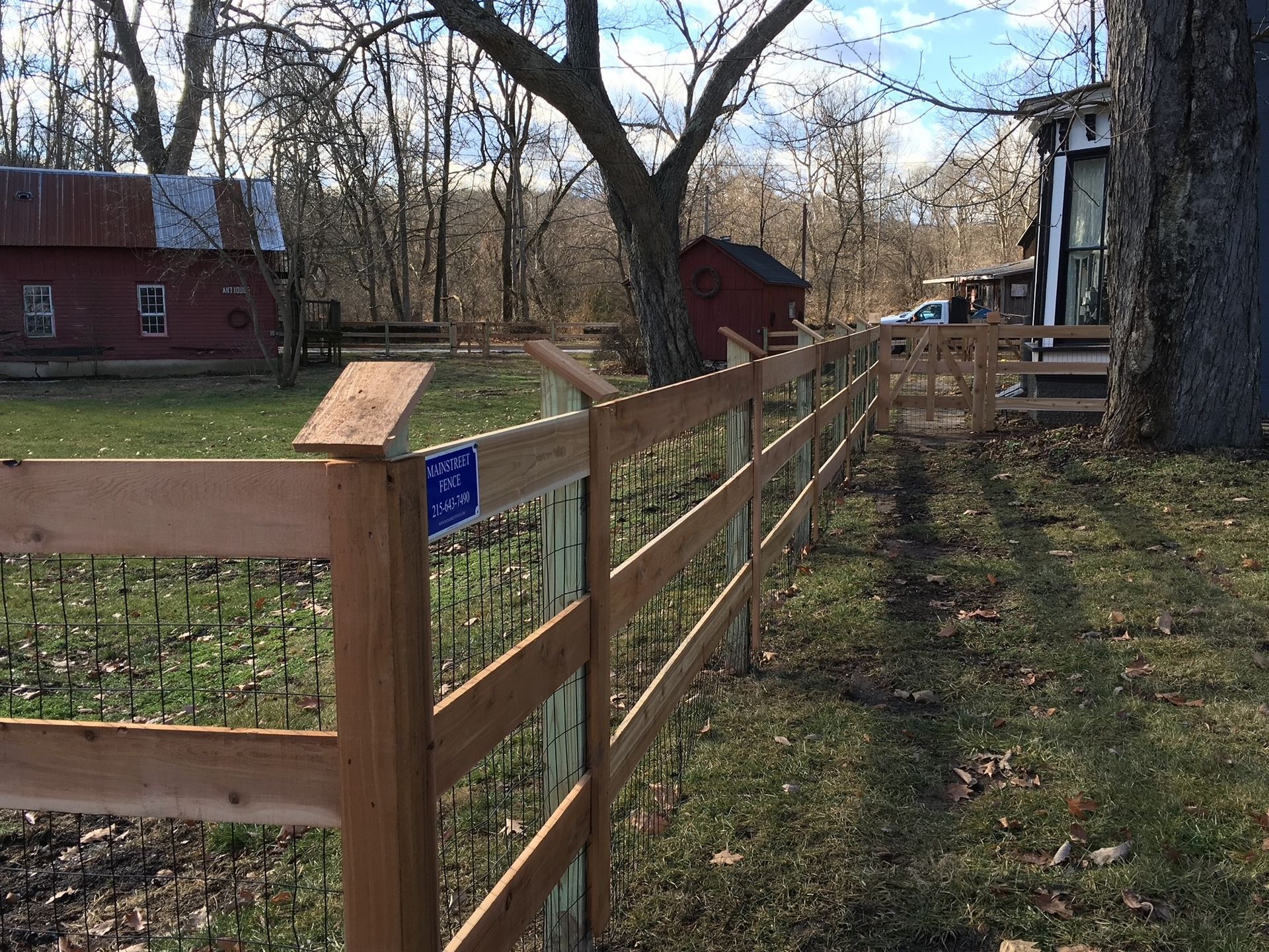 A wooden fence surrounds a grassy field with a red barn in the background.