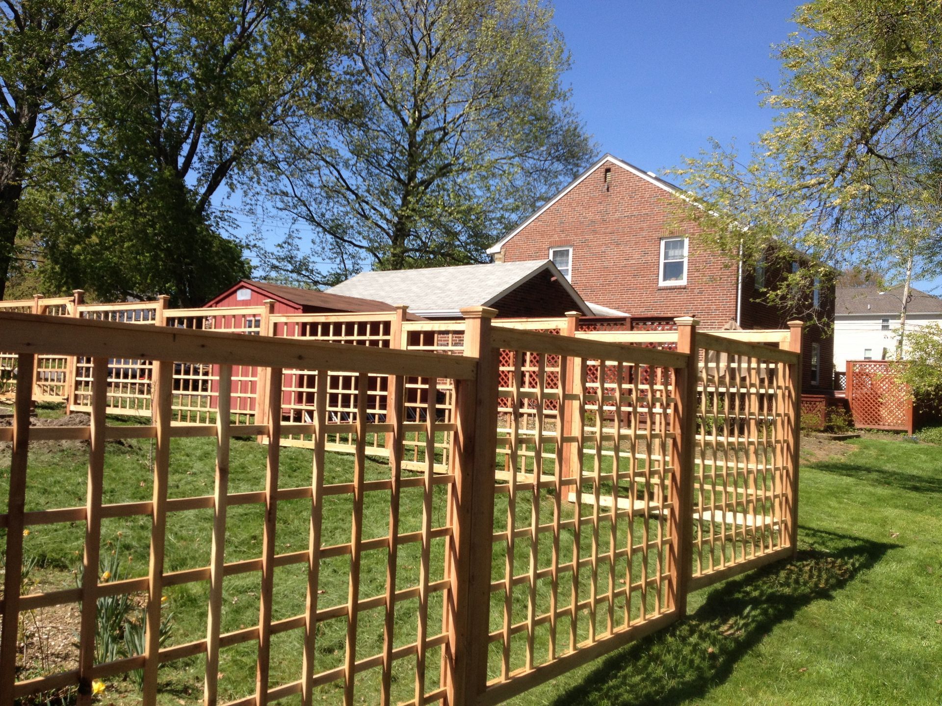 A wooden fence surrounds a lush green yard in front of a brick house.