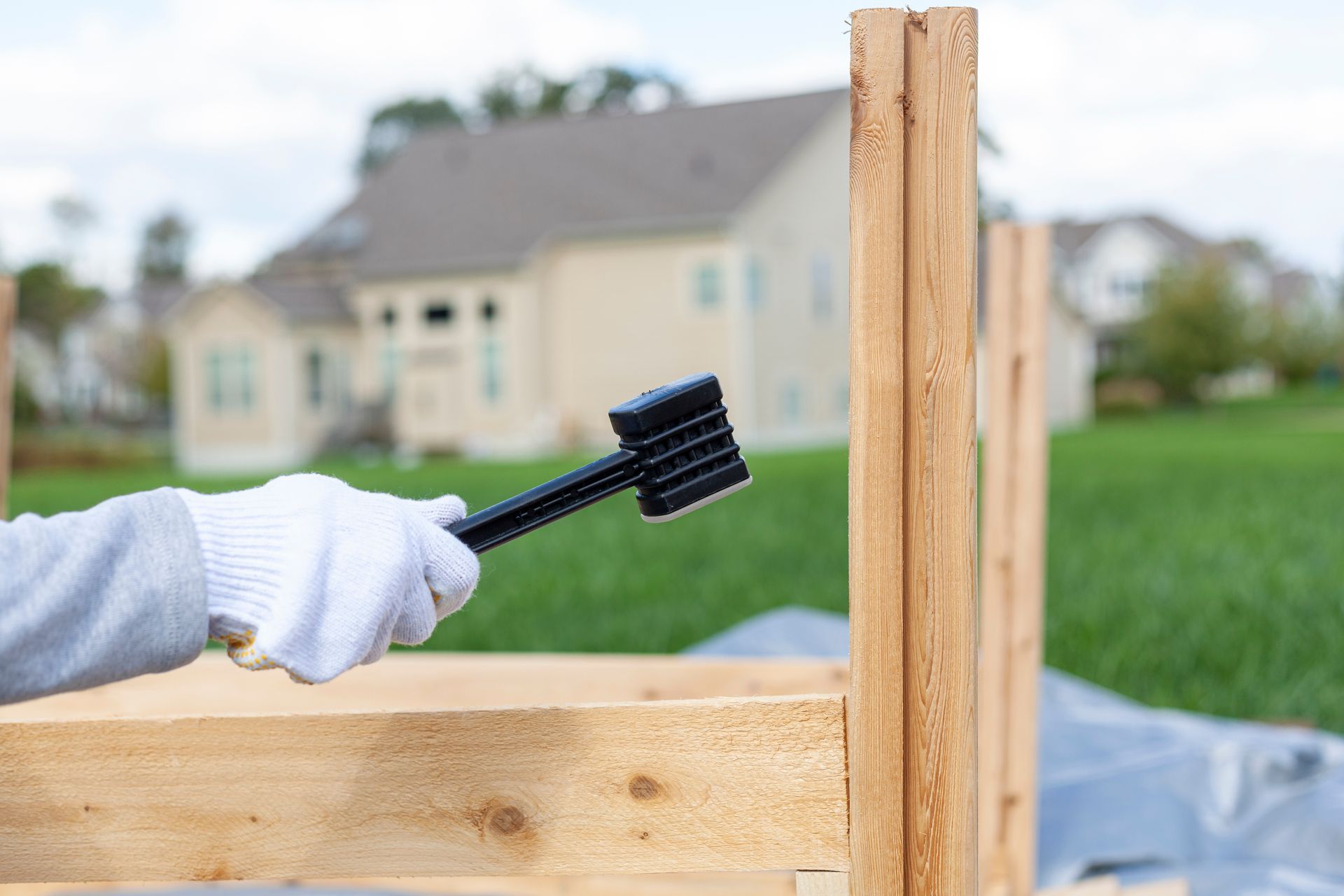 A person wearing safety gloves is installing a wooden fence using a plastic hammer to tighten.