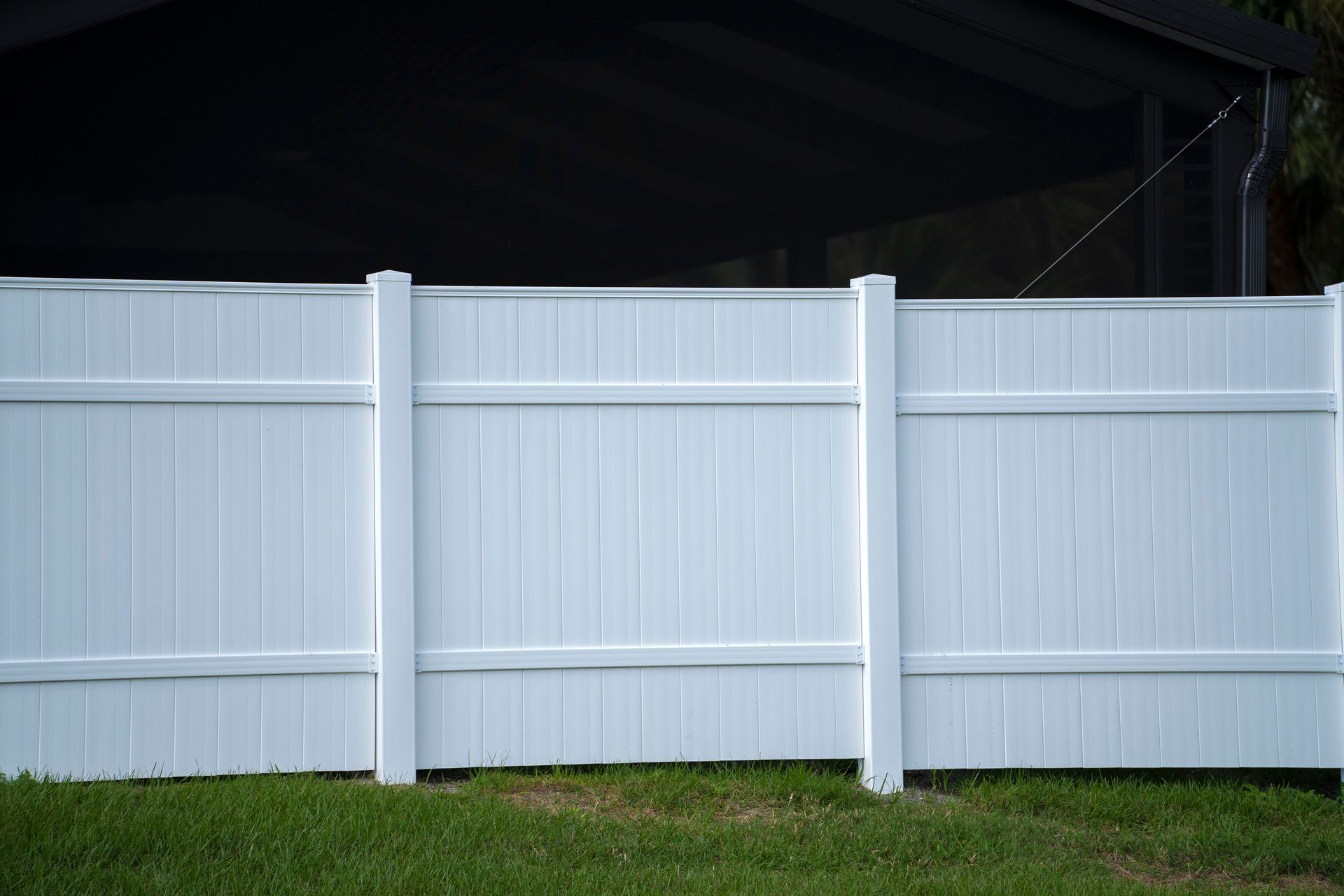 White vinyl fence on a green lawn surrounding property grounds for backyard protection and privacy.