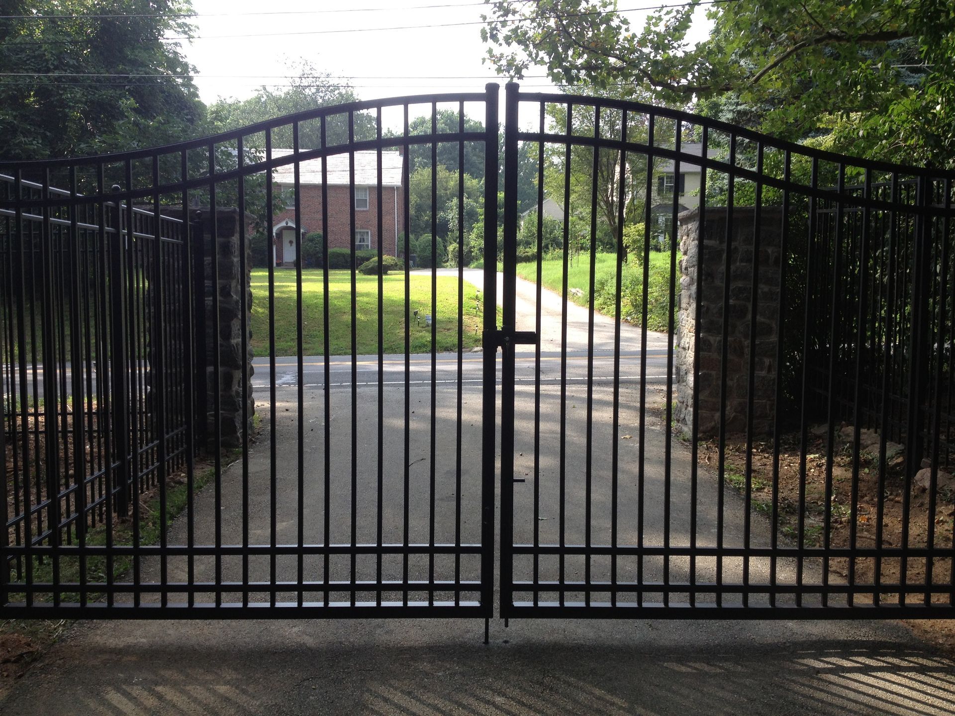 A black gate is open to a driveway leading to a house