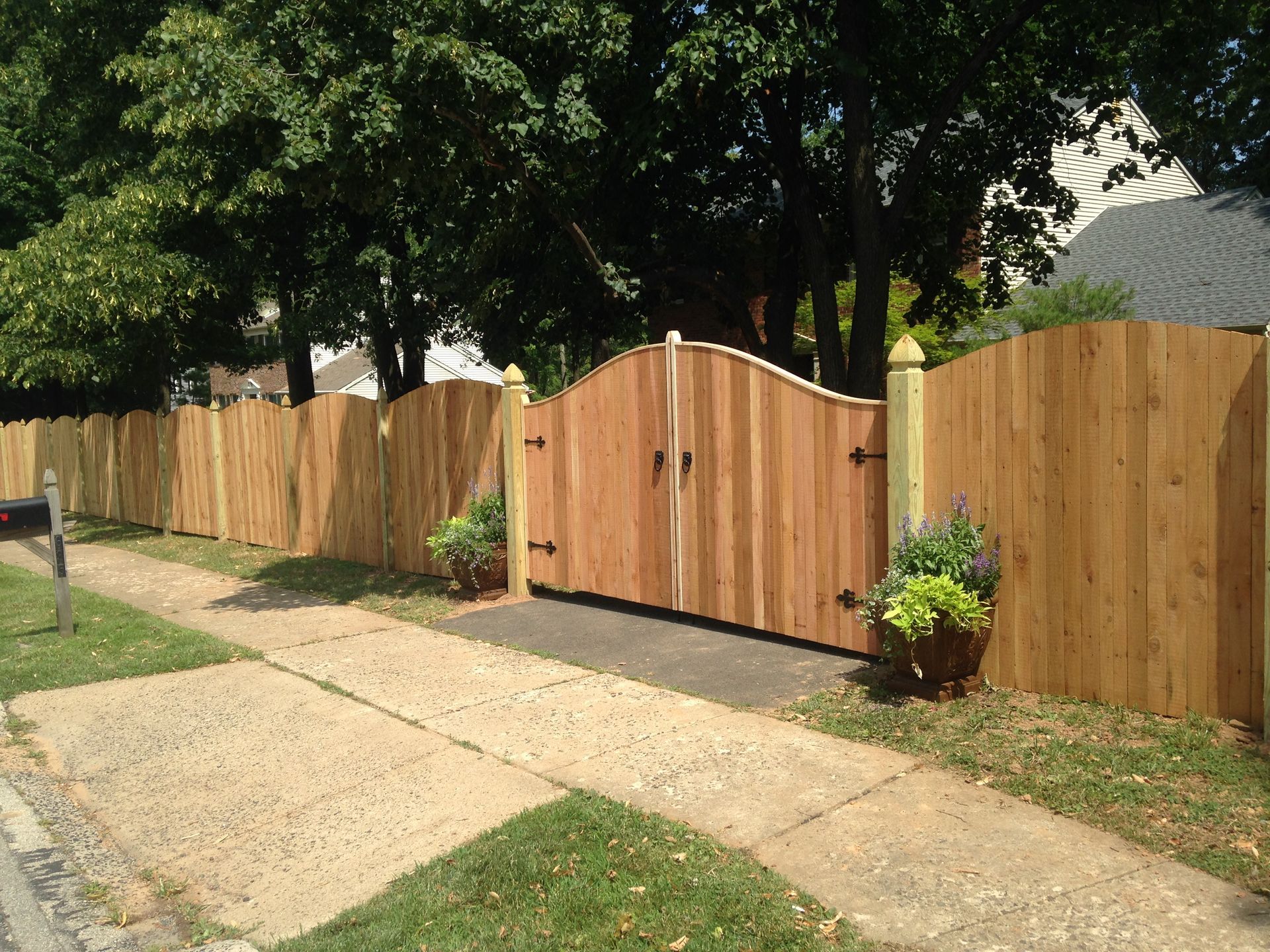 A wooden fence surrounds a driveway with trees in the background