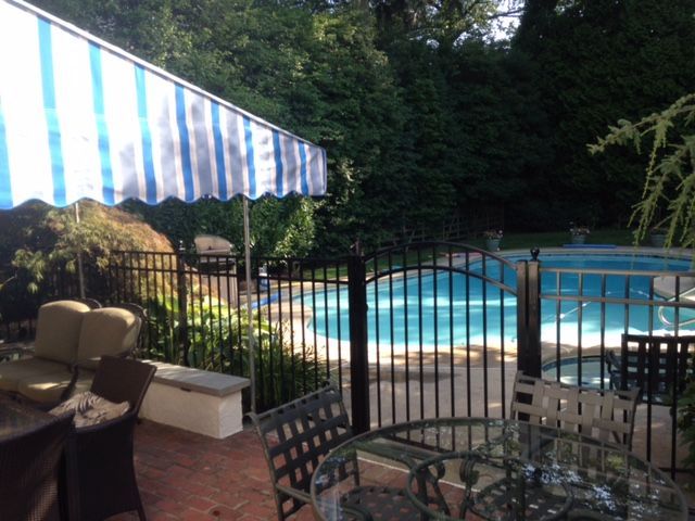 A blue and white striped awning over a patio with a pool in the background