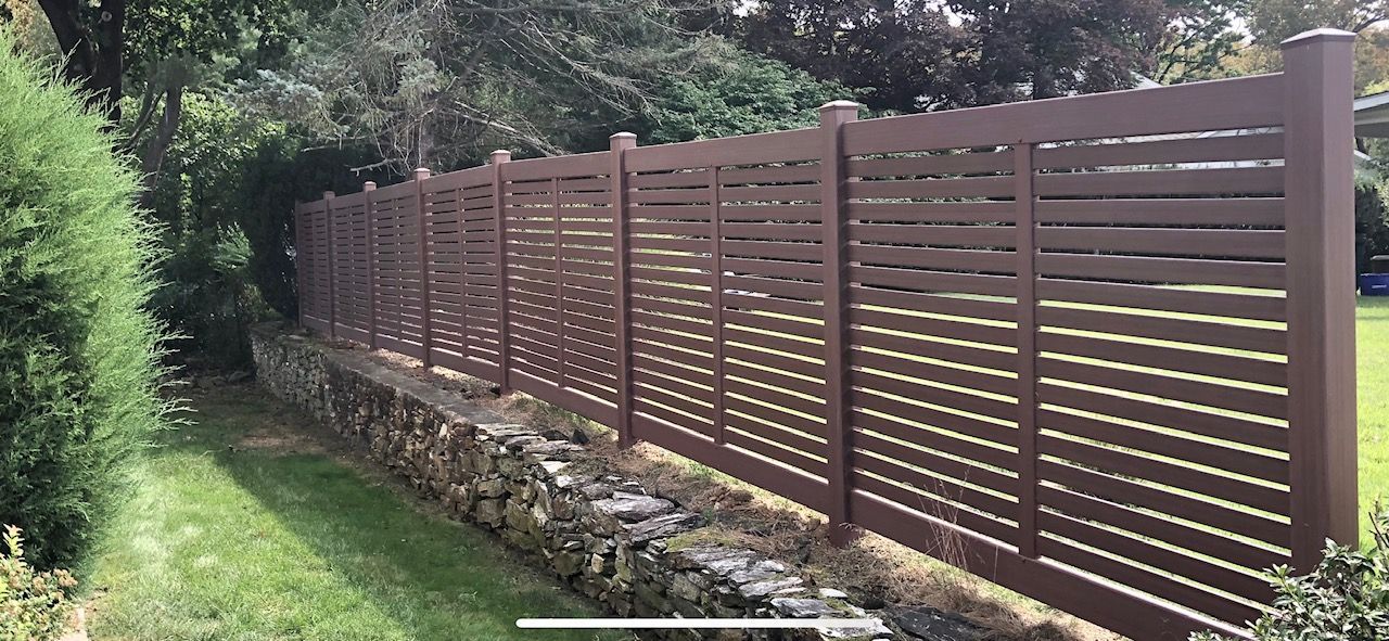 A wooden fence is surrounded by trees and grass in a yard.