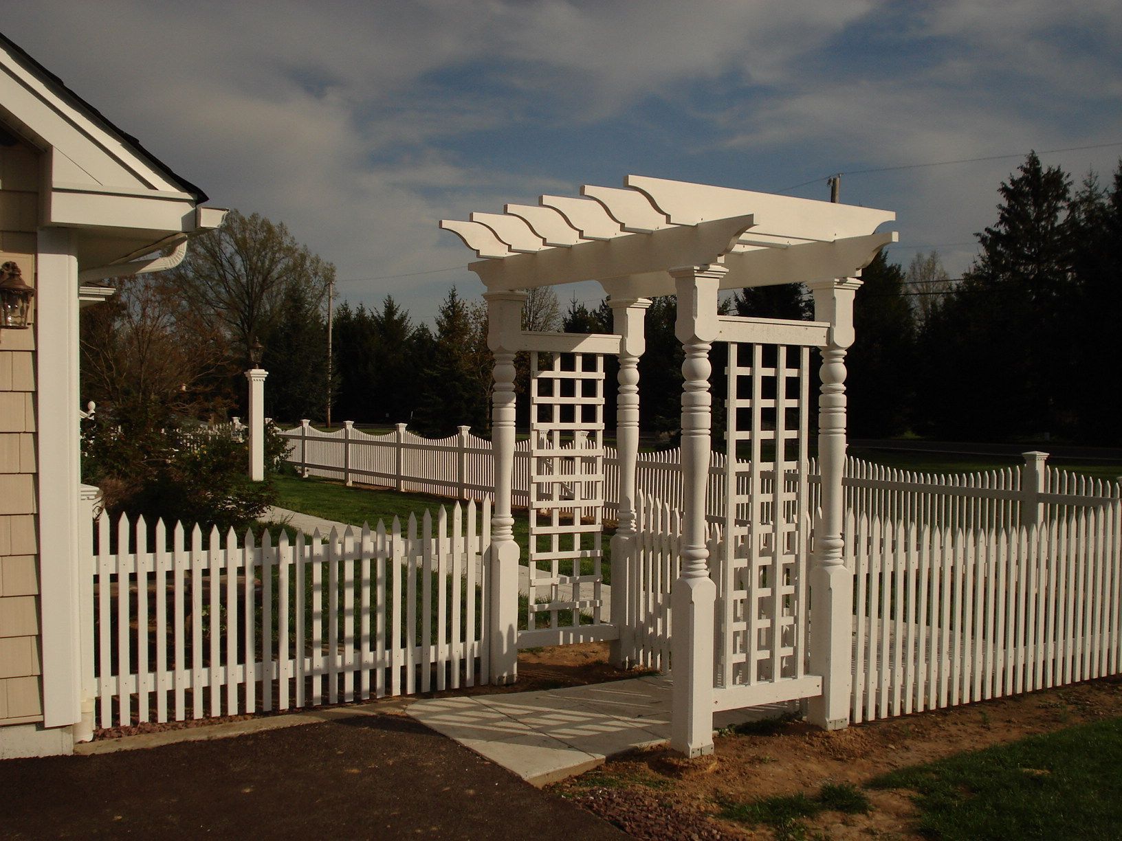 A white picket fence with a pergola in the background