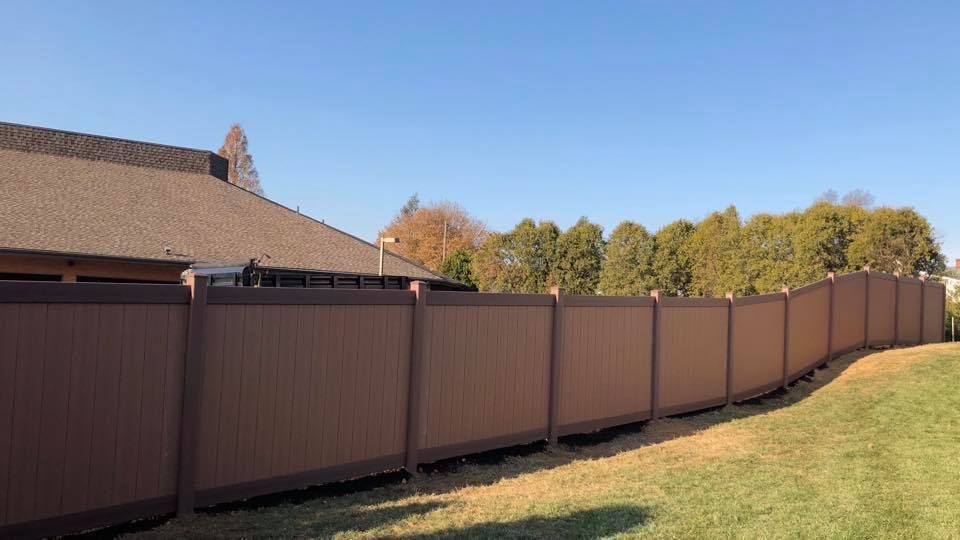 A brown fence is sitting on top of a lush green field next to a house.
