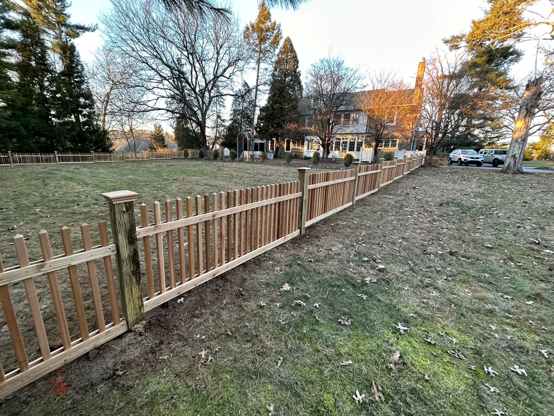 A wooden picket fence surrounds a grassy field in front of a house.