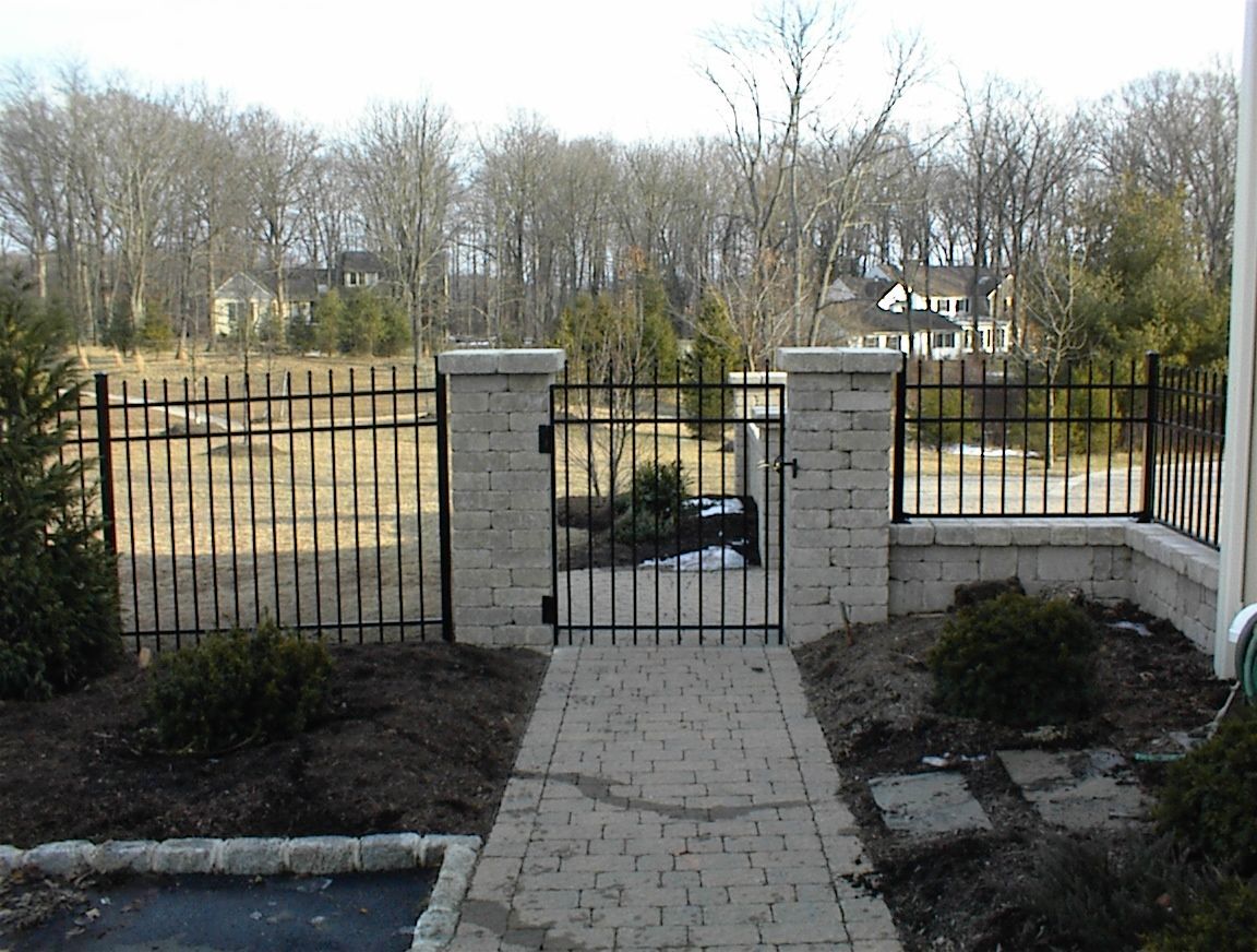 A brick walkway leading to a wrought iron gate