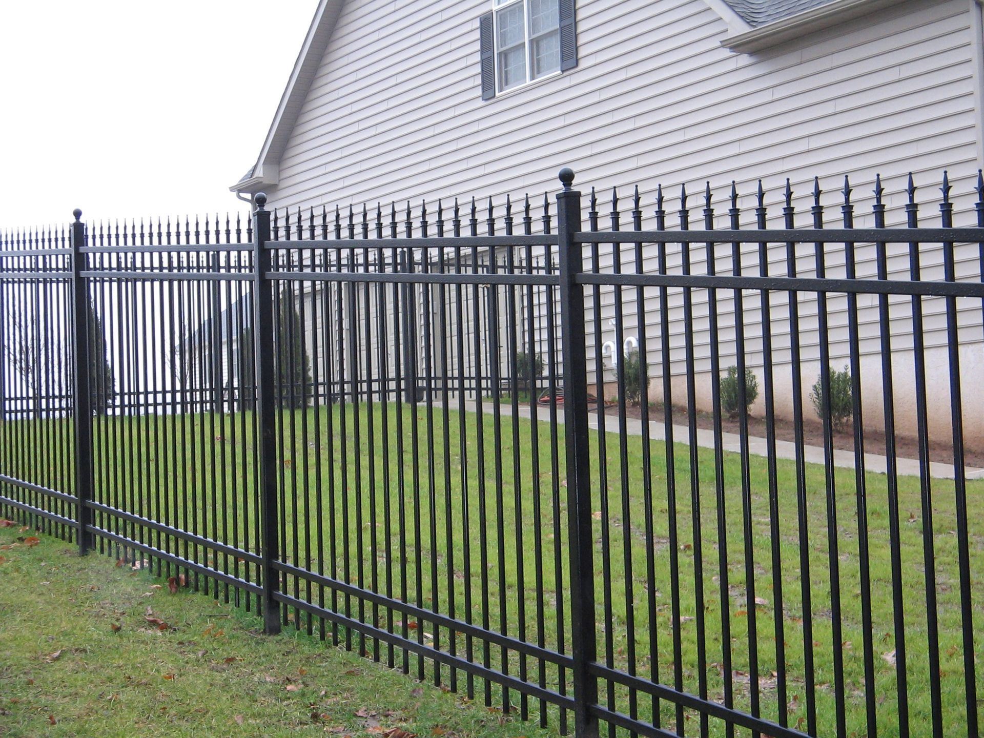 A black metal fence surrounds a lush green yard in front of a house.