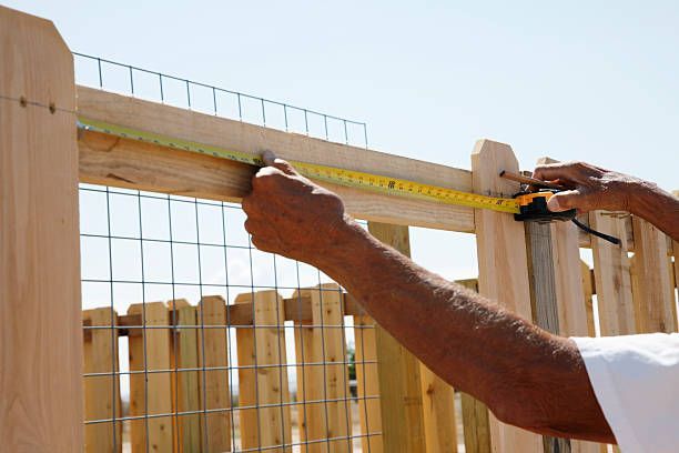 A man measures a fence with a tape measure in preparation for cedar fence installation.