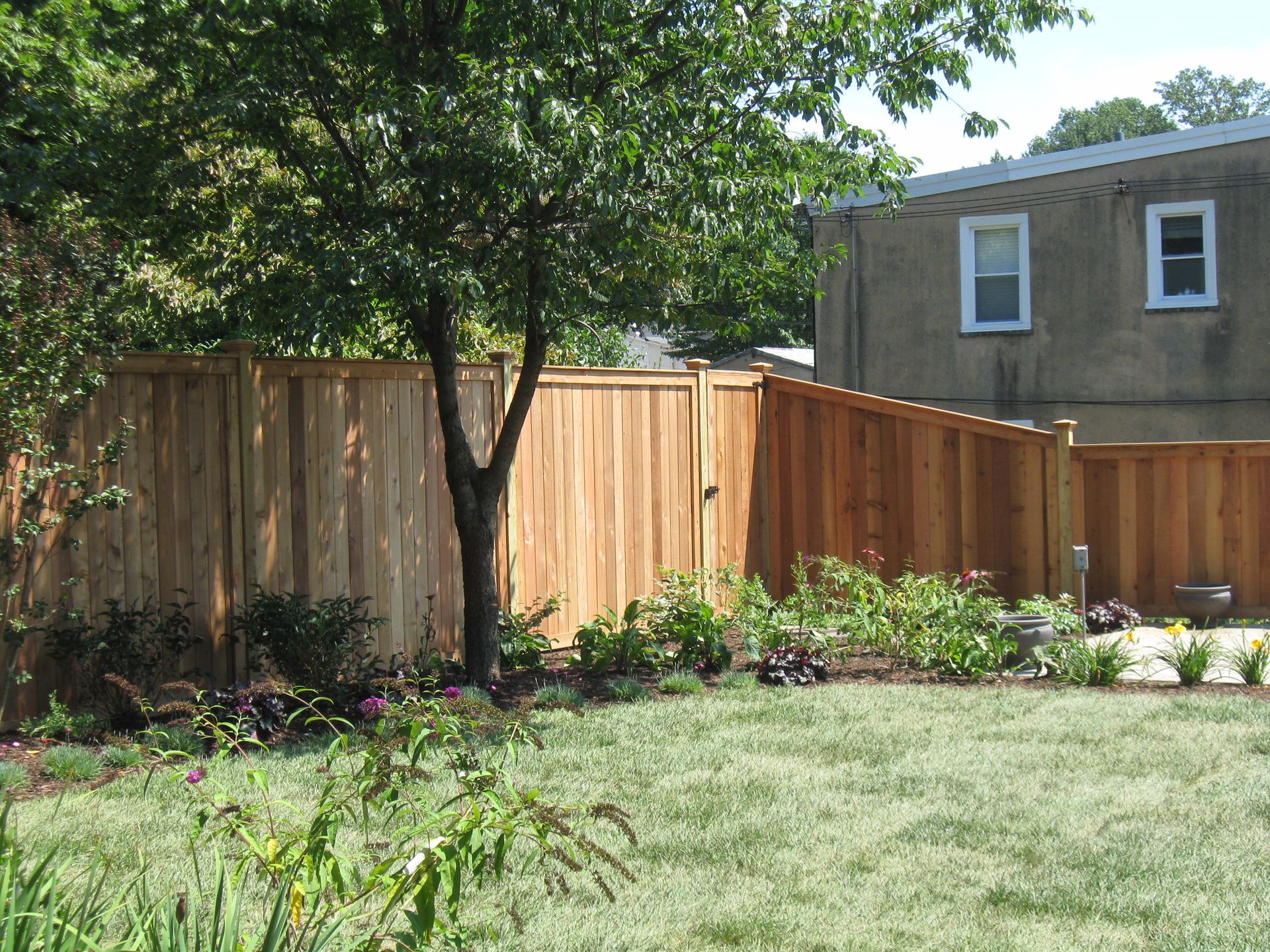 A wooden fence surrounds a lush green yard in front of a house.