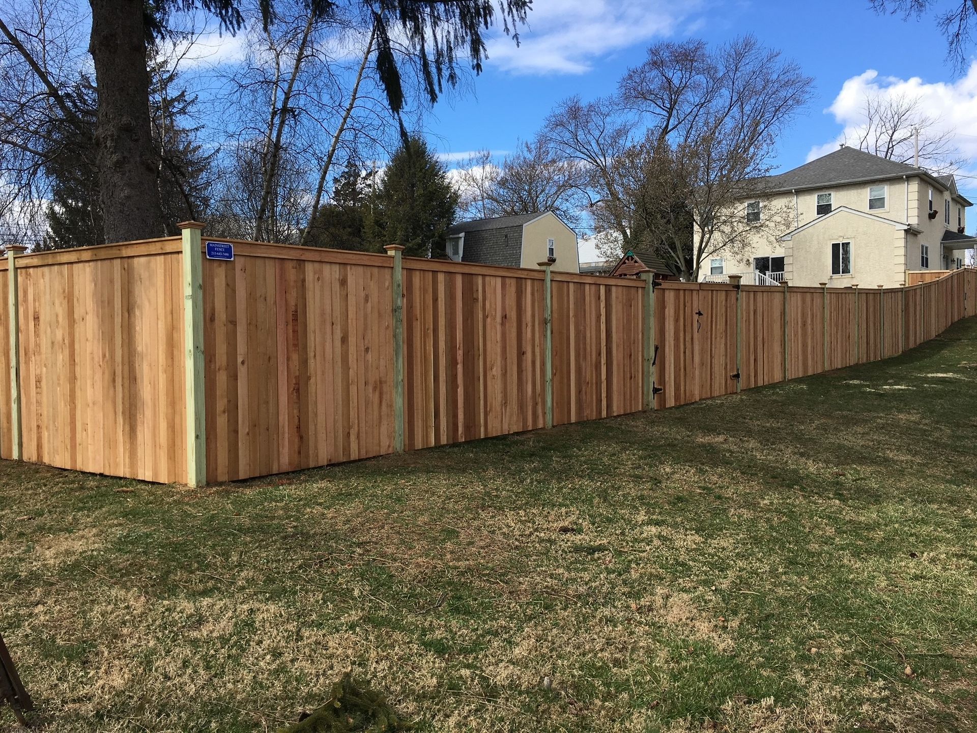 A wooden fence surrounds a lush green yard in front of a house.