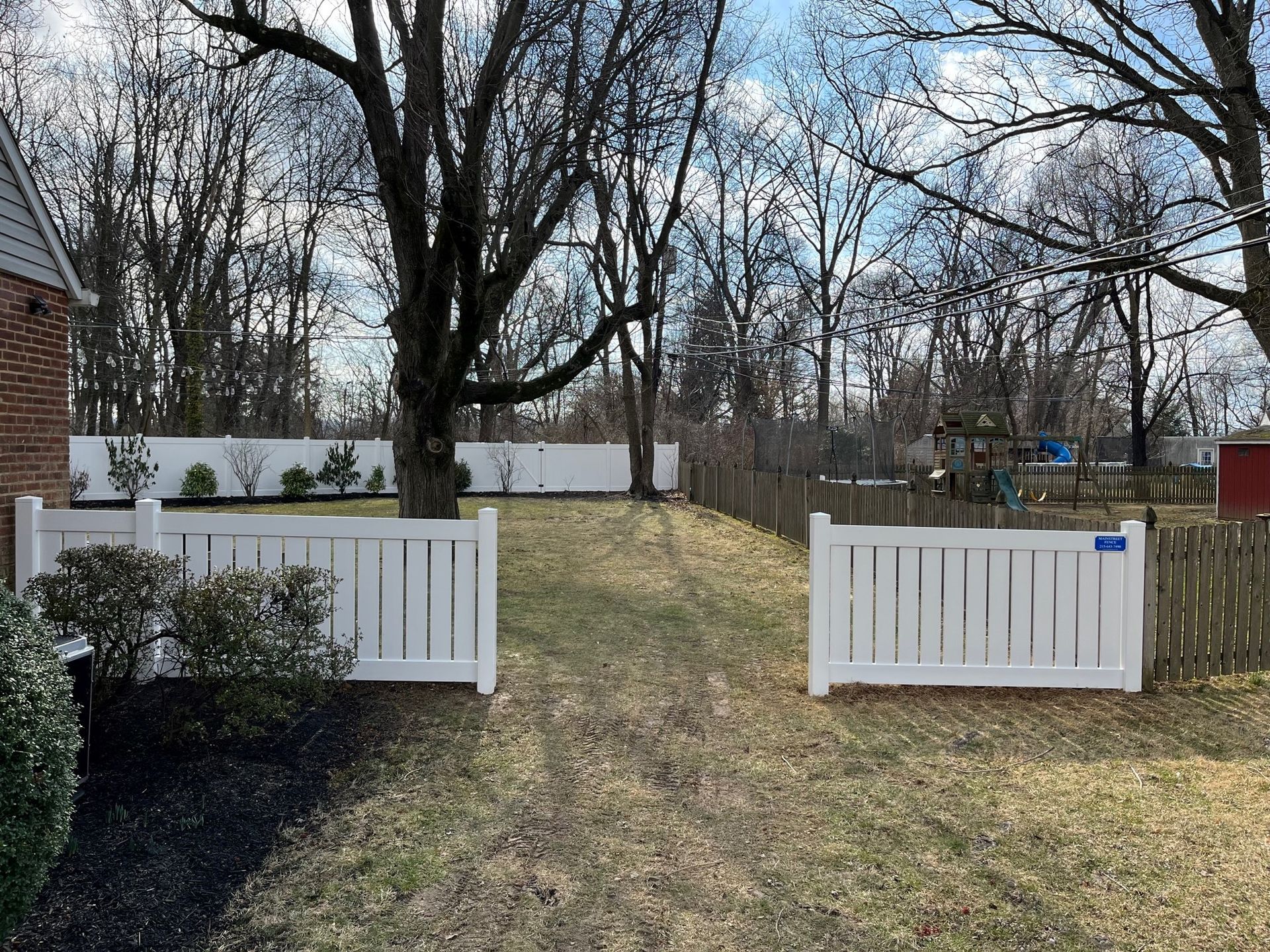 A white fence surrounds a yard with trees in the background.