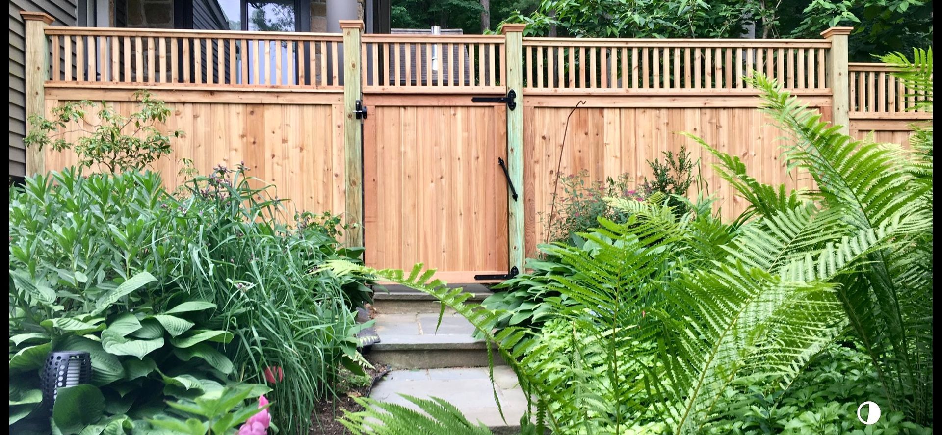 A wooden fence with a gate in the middle of a garden.