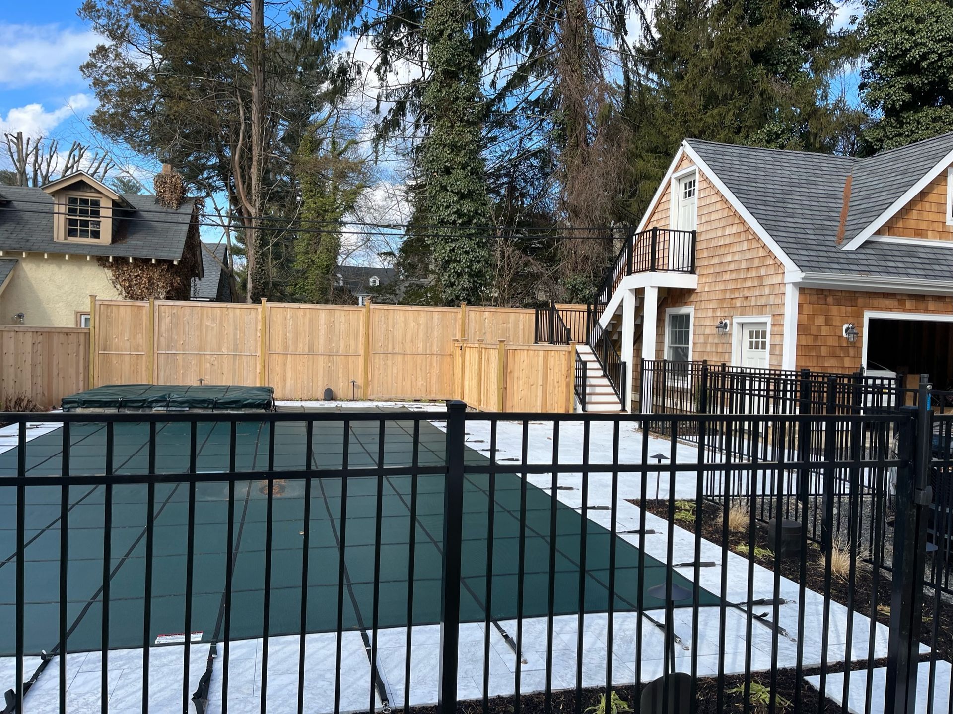 A fence surrounds a swimming pool in front of a house.