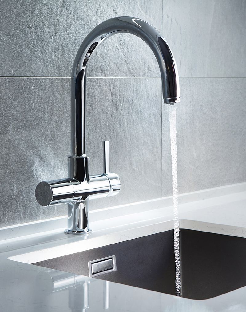 Chrome faucet with water running into a dark sink, set against a gray tiled wall.