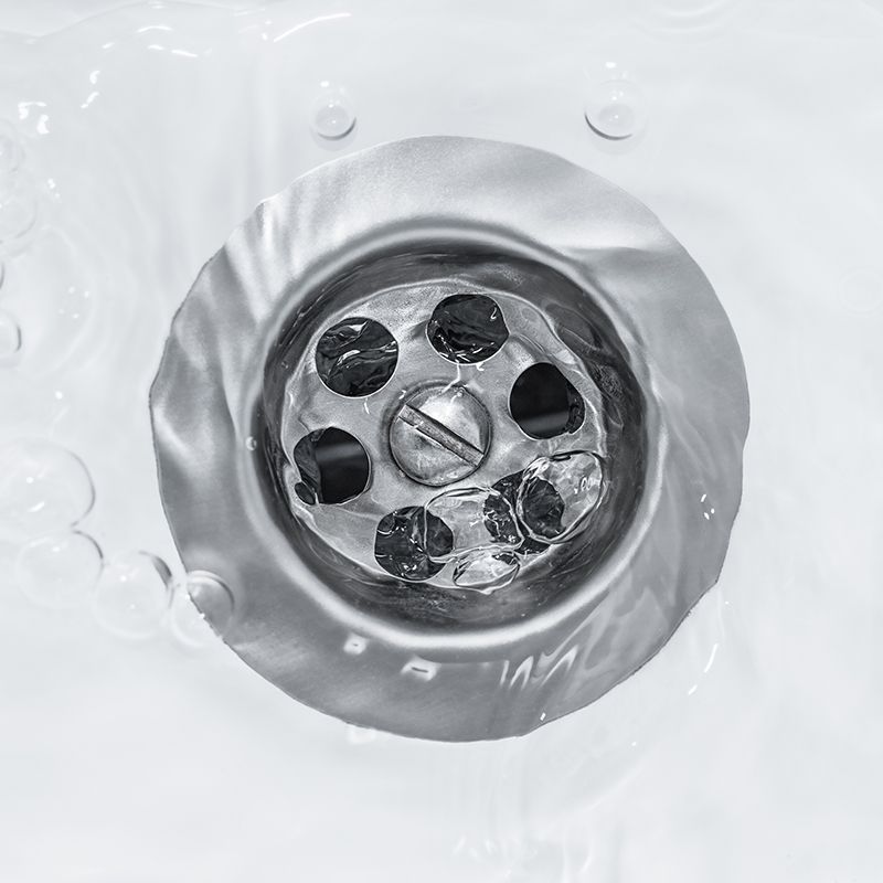Water flowing into a silver sink drain, close-up view.