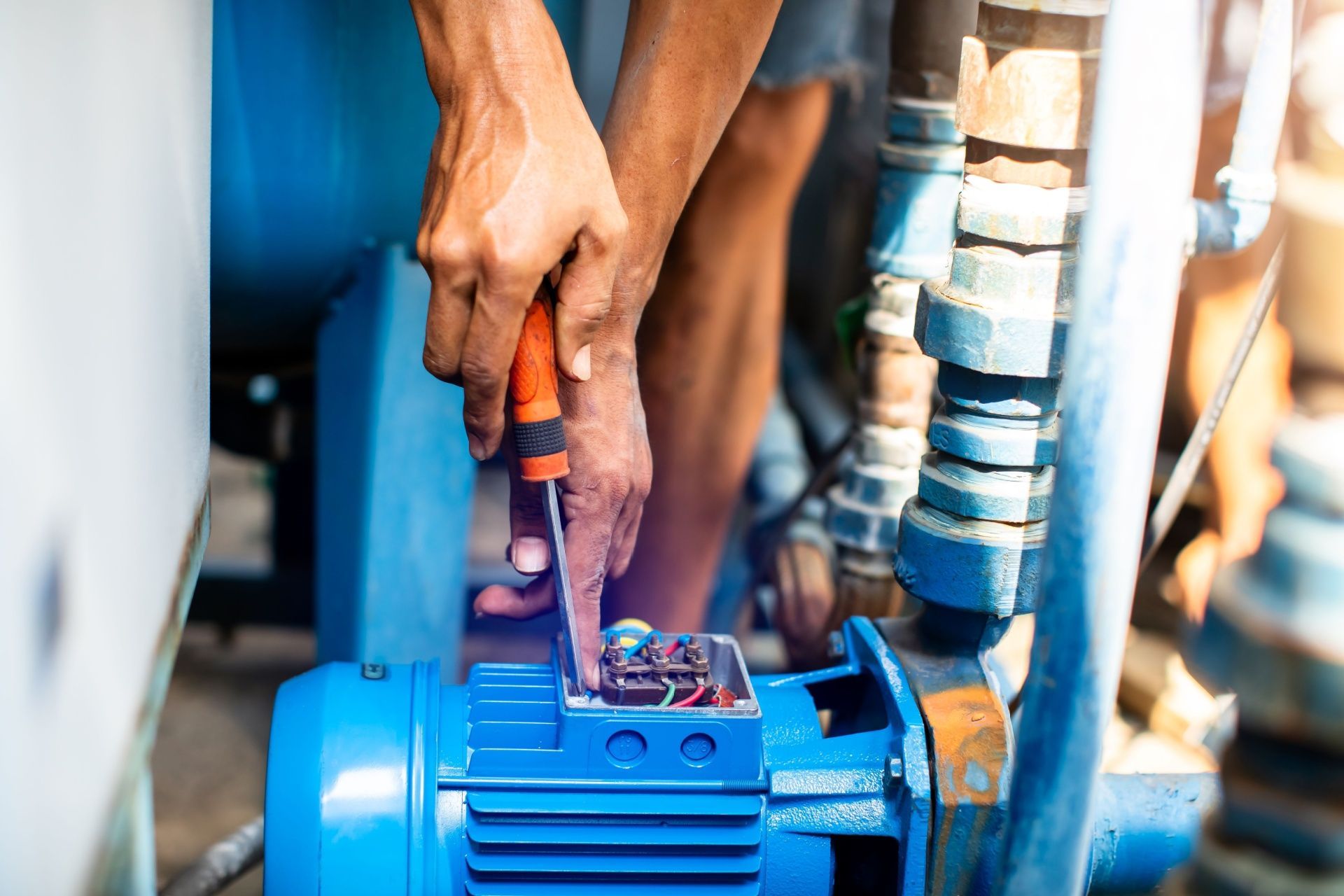 Person repairs a blue water pump with a screwdriver, outdoors.
