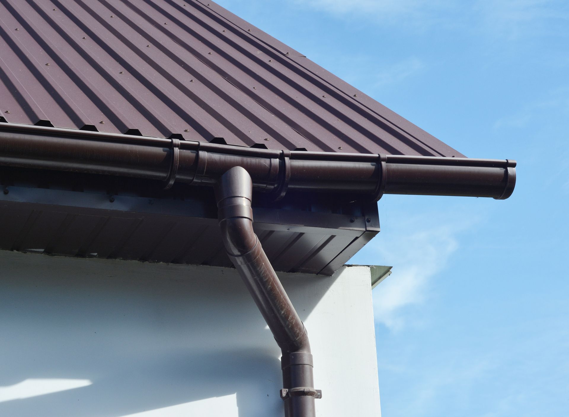 Brown metal roof with fascia, soffit, and rain gutter on a white wall under the sky. Brown metal roof with fascia, soffit, and rain gutter on a white wall under the sky.