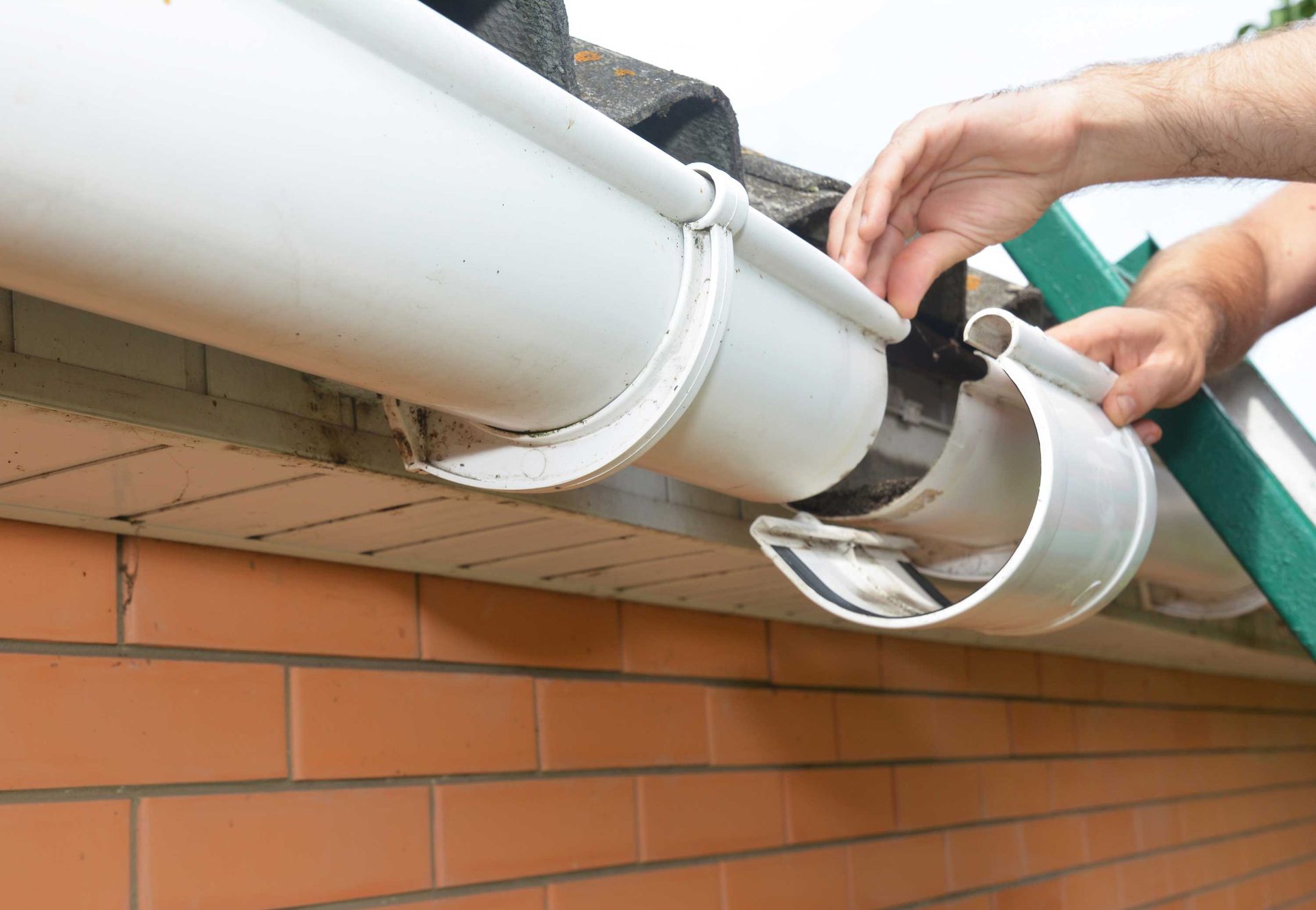 Gutter repair connecting downspout sections on brick exterior wall.