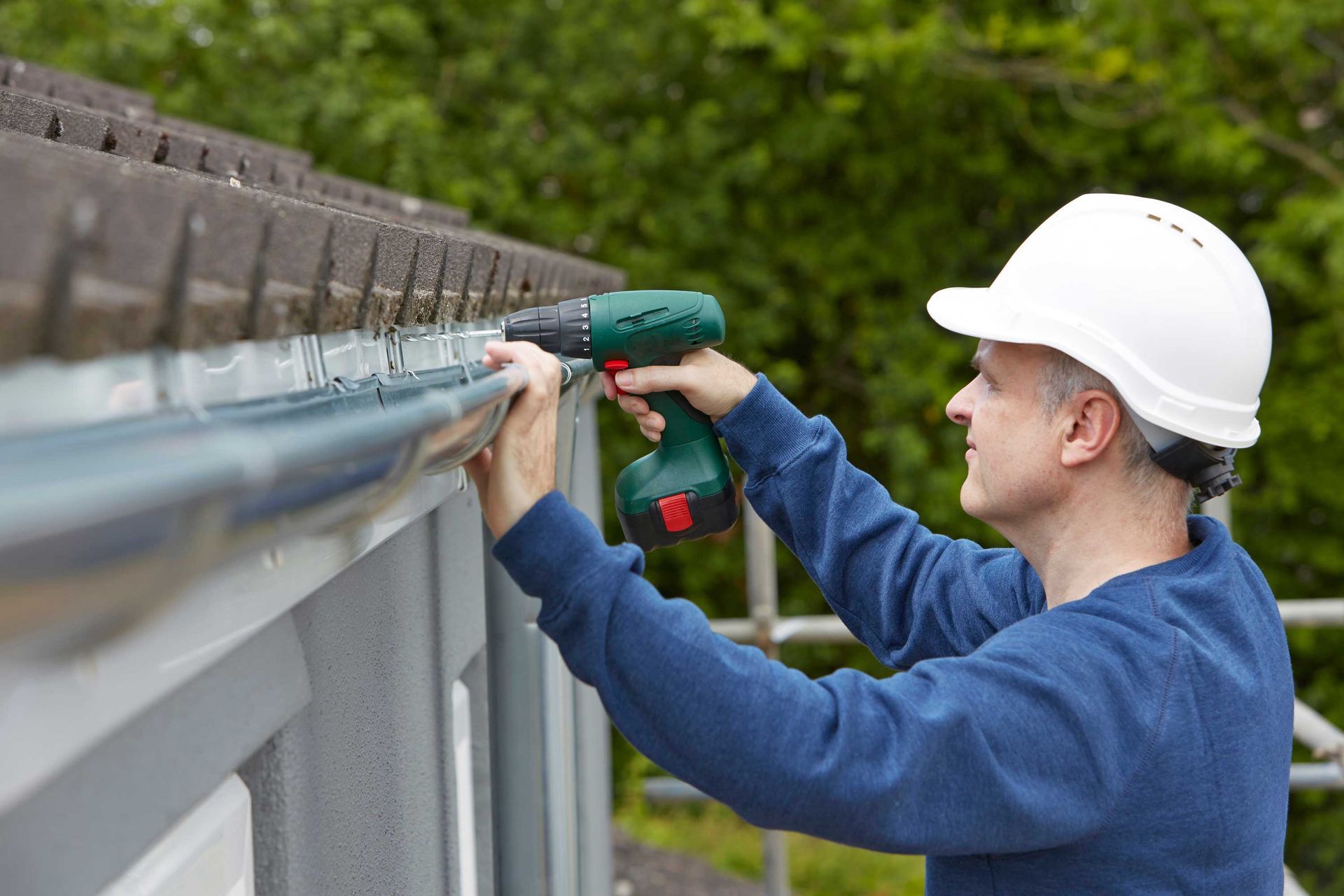 A technician installing residential gutters with a power drill.